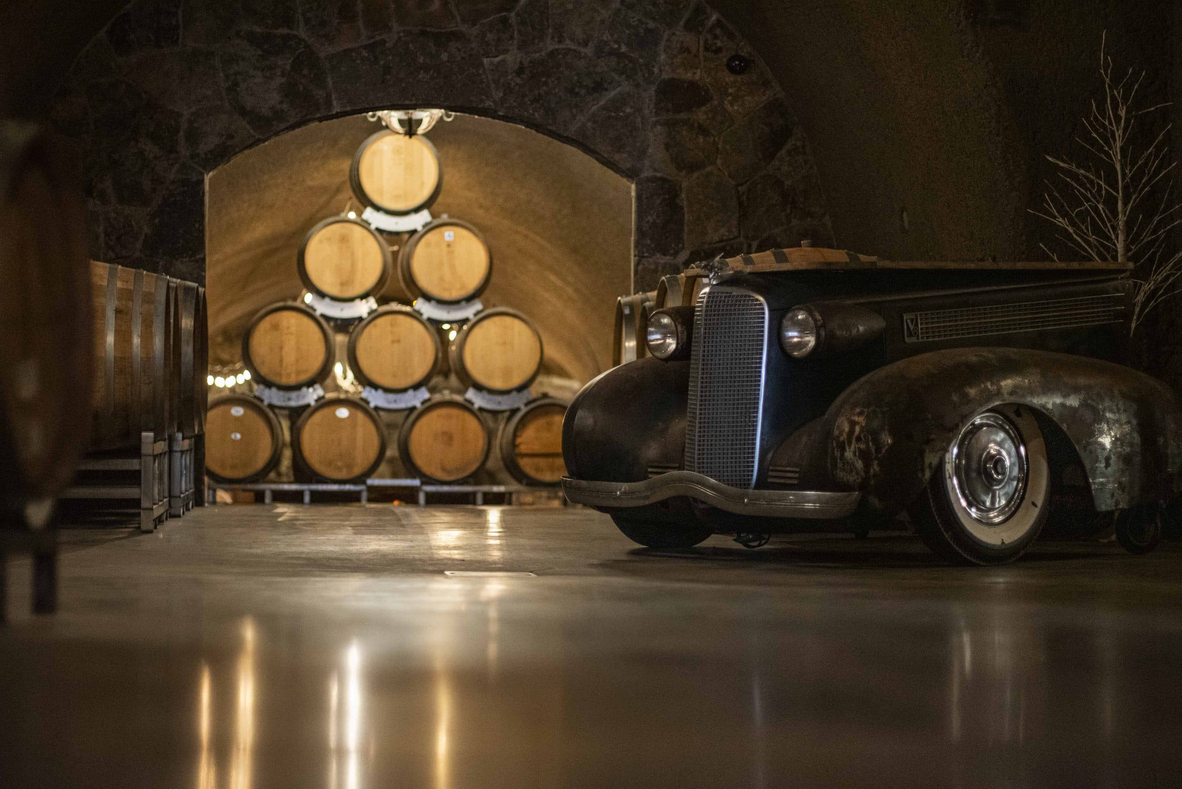 Barrels stacked in the Joseph Cellars wine cave beside a vintage car